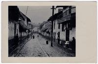 “A typical street of this city, showing houses with thatched roofs and the open sewerage system still used here”